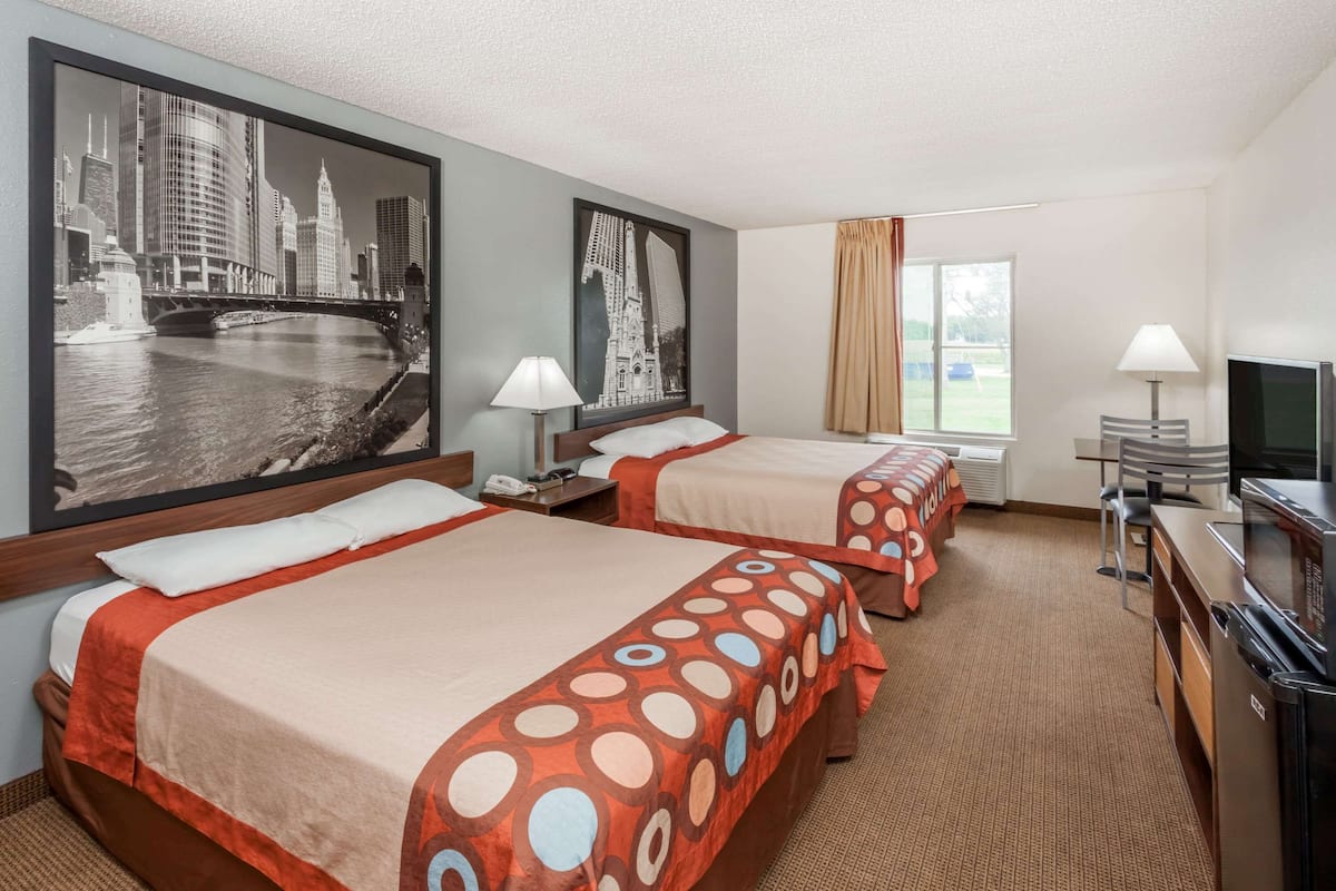 A hotel room with two beds, a television, a desk, and a large window.