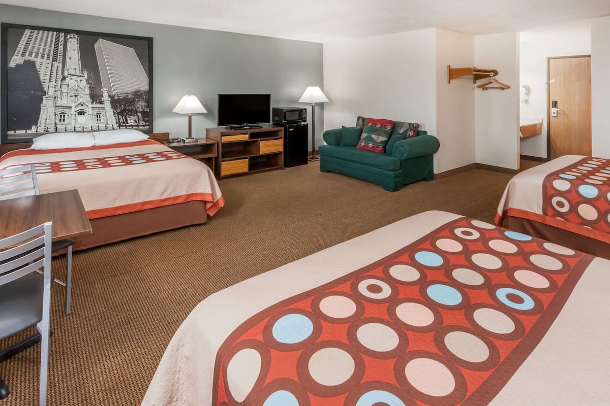 A hotel room with two beds, a TV, a desk, a lamp, a couch, and a large poster on the wall.