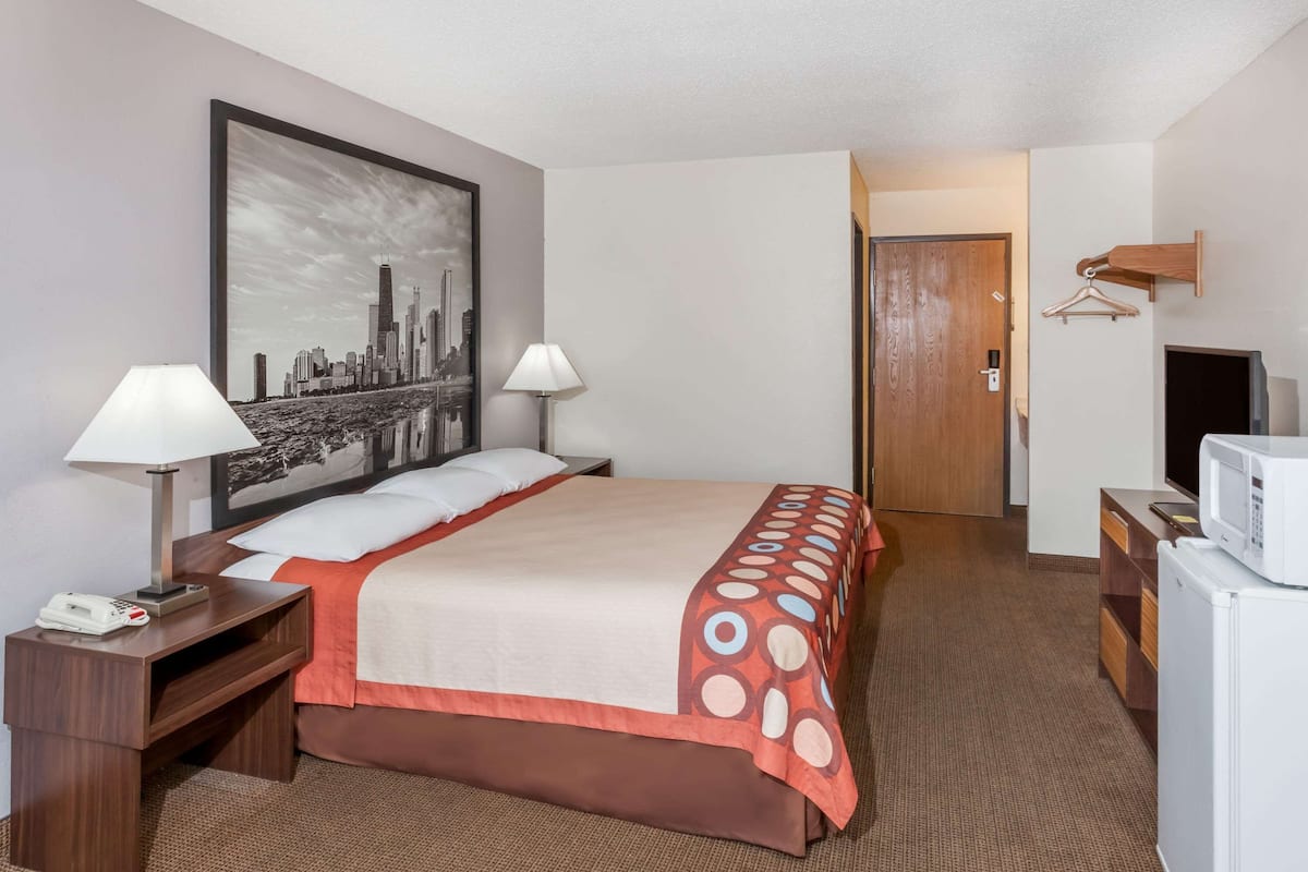 A hotel room with a bed, two bedside lamps, a telephone, a television, and a microwave.