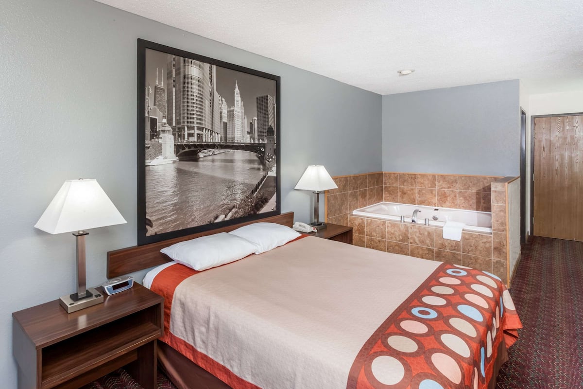 A hotel room with a large bed, two bedside lamps, a nightstand, a wall-mounted TV, and a bathroom with a bathtub and sink.