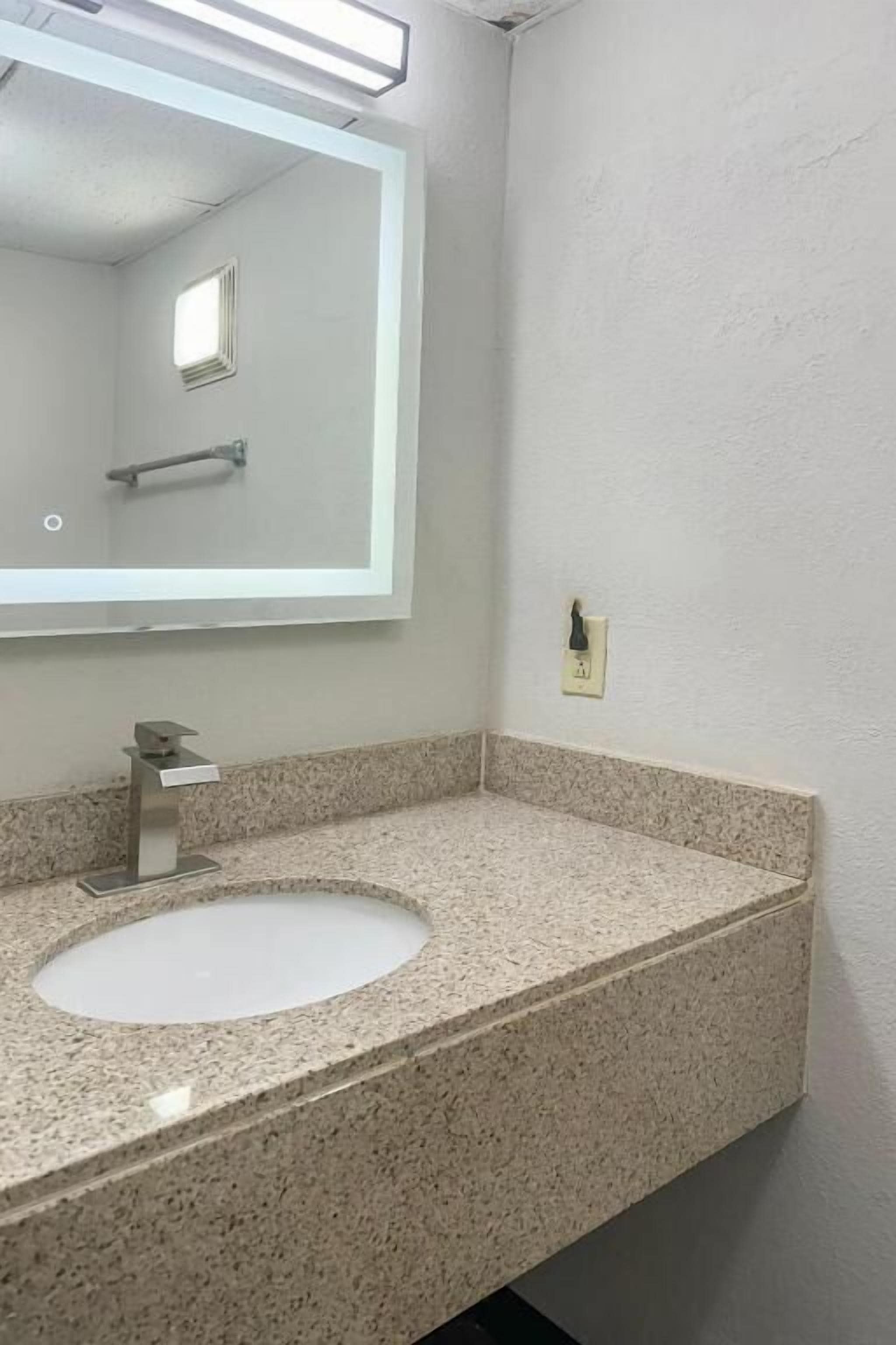 Ein Badezimmer mit Granitwaschtisch, Waschbecken, Spiegel und einer Leuchte.