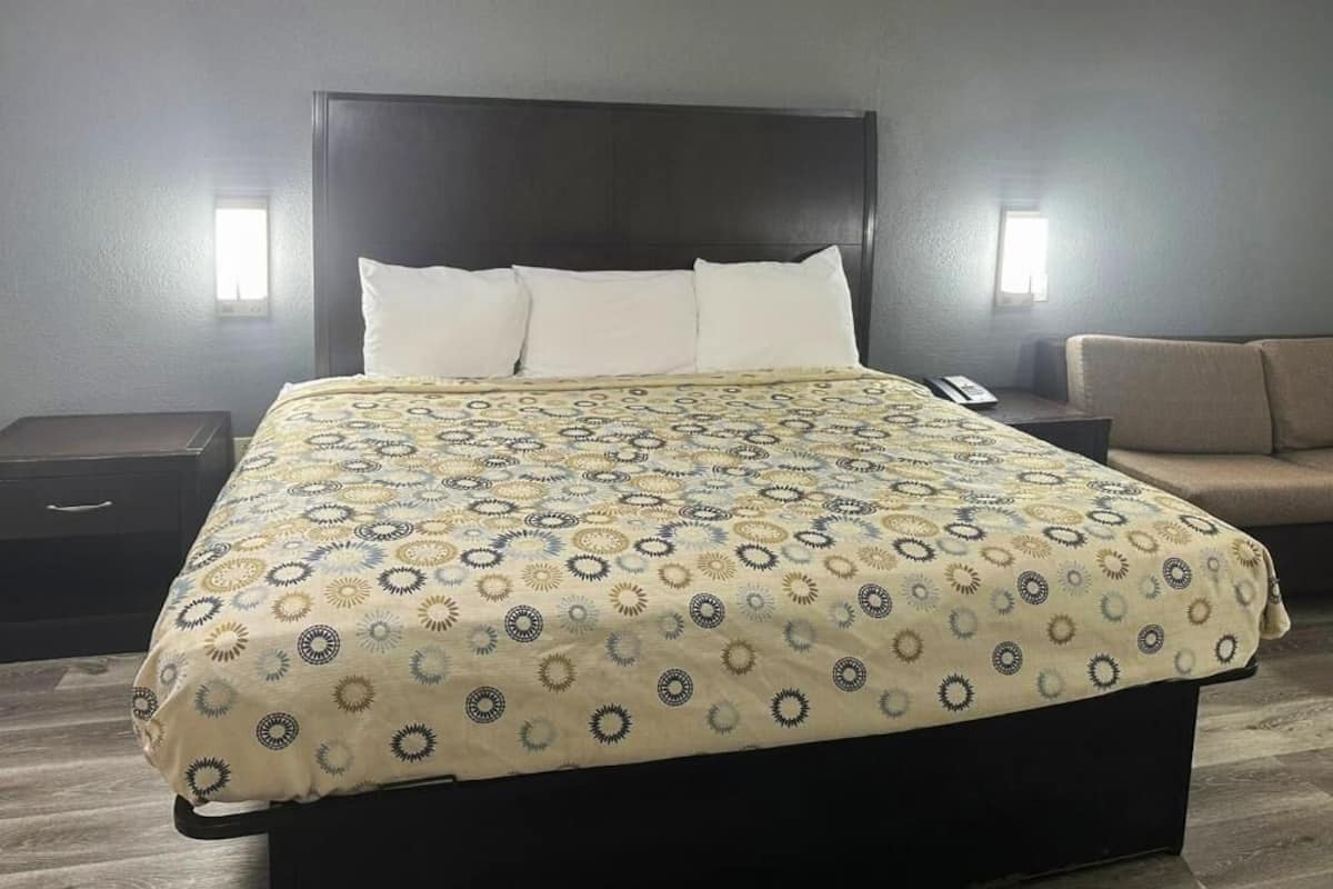A hotel room with a large bed, a bedside table, a nightstand, and a sofa.