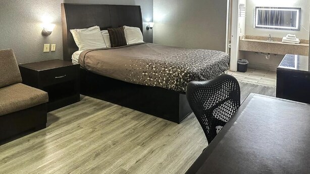 A modern hotel room with a bed, a sofa, a dining table, and a bathroom with a sink and mirror. - Regal Inn Guntersville Hwy 431 (Guntersville)