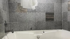 A modern bathroom with a freestanding bathtub, grey stone tiles, a showerhead, and a ceiling light fixture. - Regal Inn Guntersville Hwy 431 (Guntersville)