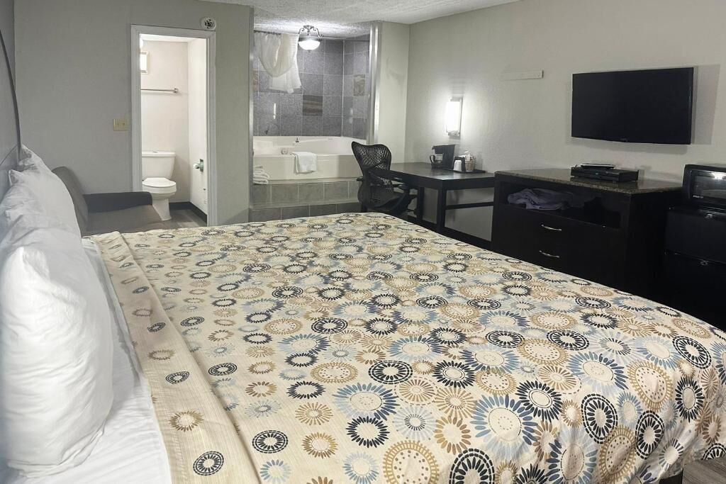 A hotel room with a bed, a desk, a TV, and a bathroom visible through an open door.