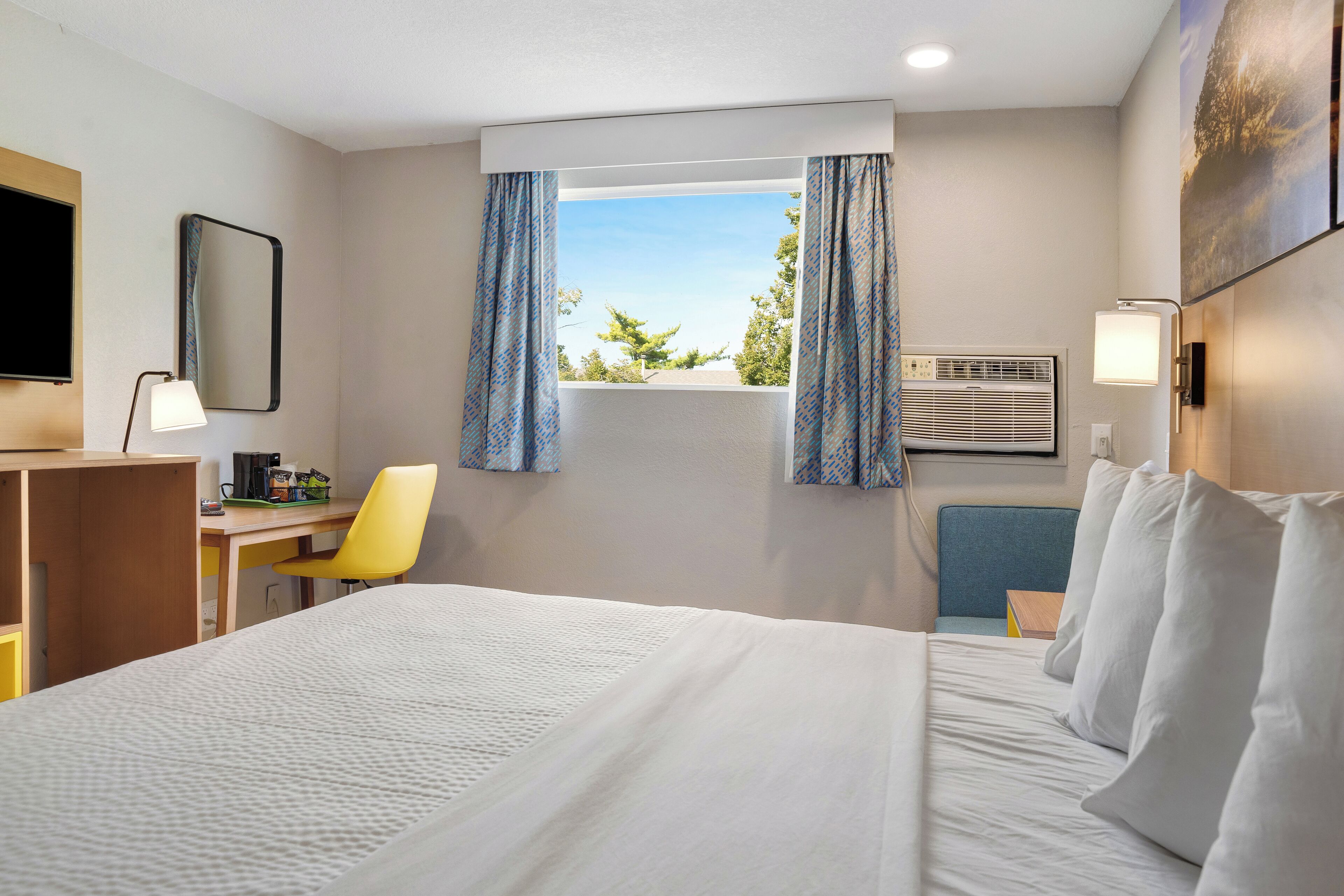 Une chambre d’hôtel avec un lit, un bureau, une chaise, une télévision et une fenêtre avec des rideaux.