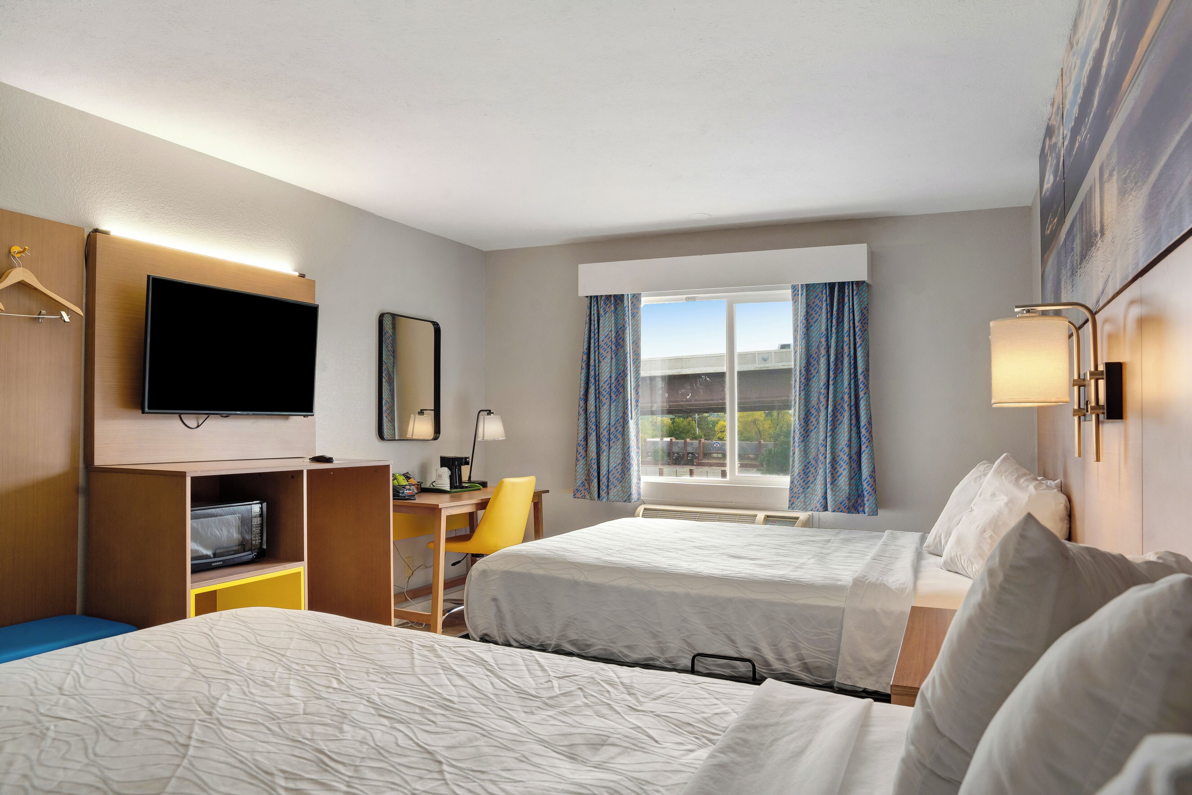 Une chambre d’hôtel avec deux lits, un bureau, une chaise, un téléviseur à écran plat et une fenêtre avec des rideaux.