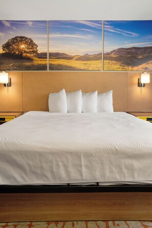 Habitación de hotel con una cama grande, dos lámparas de pared y un cuadro de paisaje sobre la cama.