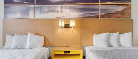 A hotel room with two beds, a wooden headboard, a nightstand, and a wall-mounted lamp.