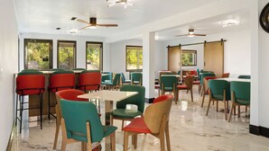 Un comedor moderno con varias mesas y sillas, ventanas amplias y ventiladores de techo.