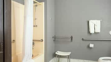 Un baño con ducha, inodoro, barras de apoyo y un taburete blanco pequeño.