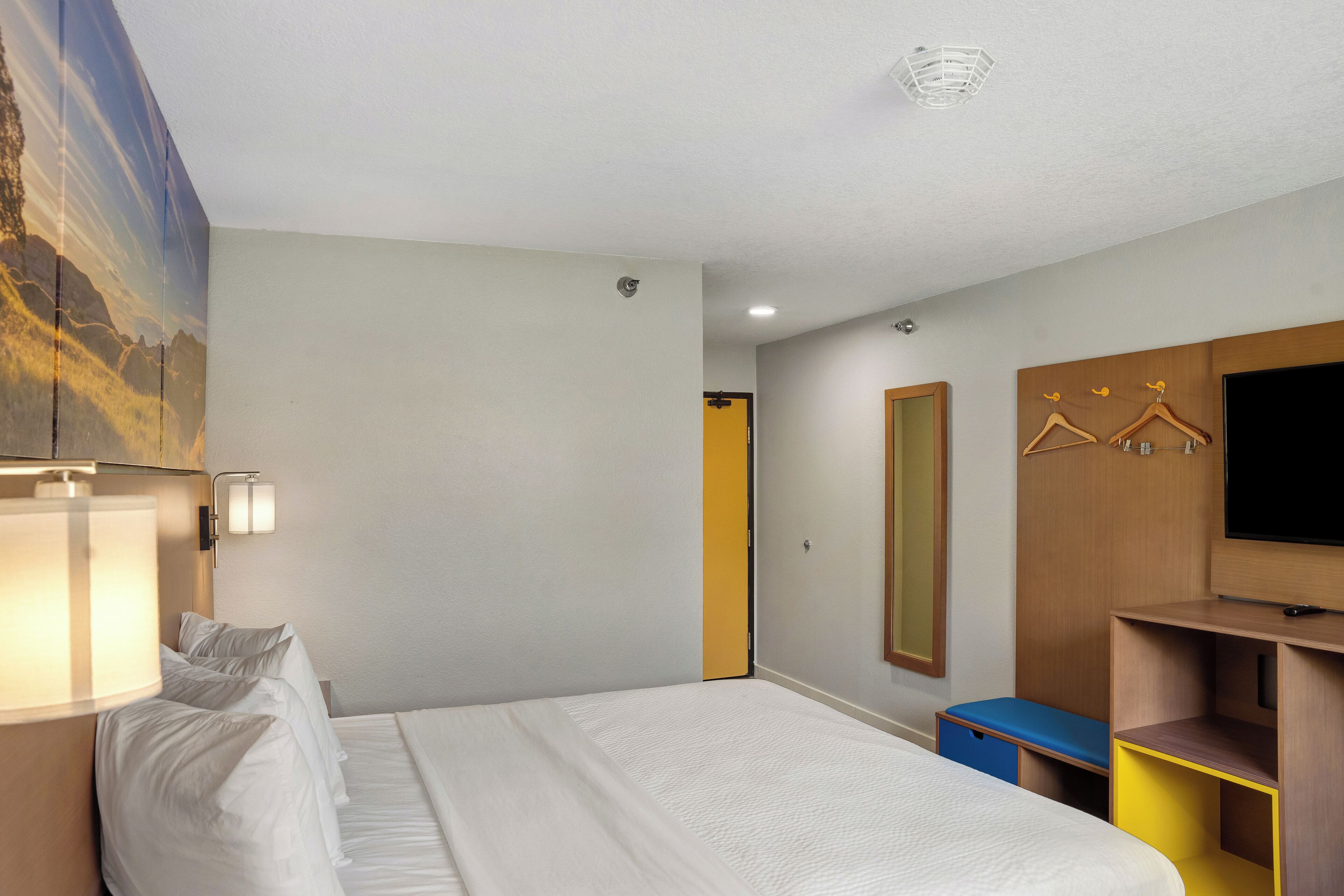 Ein Hotelzimmer mit einem Bett, Nachttischlampen, einem Fernseher, einem Kleiderschrank und einem Spiegel.