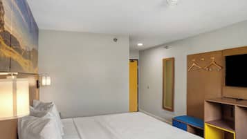 Ein Hotelzimmer mit einem Bett, Nachttischlampen, einem Fernseher, einem Kleiderschrank und einem Spiegel.