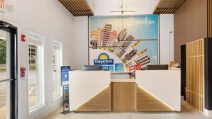 Zona de recepción con el letrero de Days Inn, un mural con vista a la ciudad y un mostrador de madera.