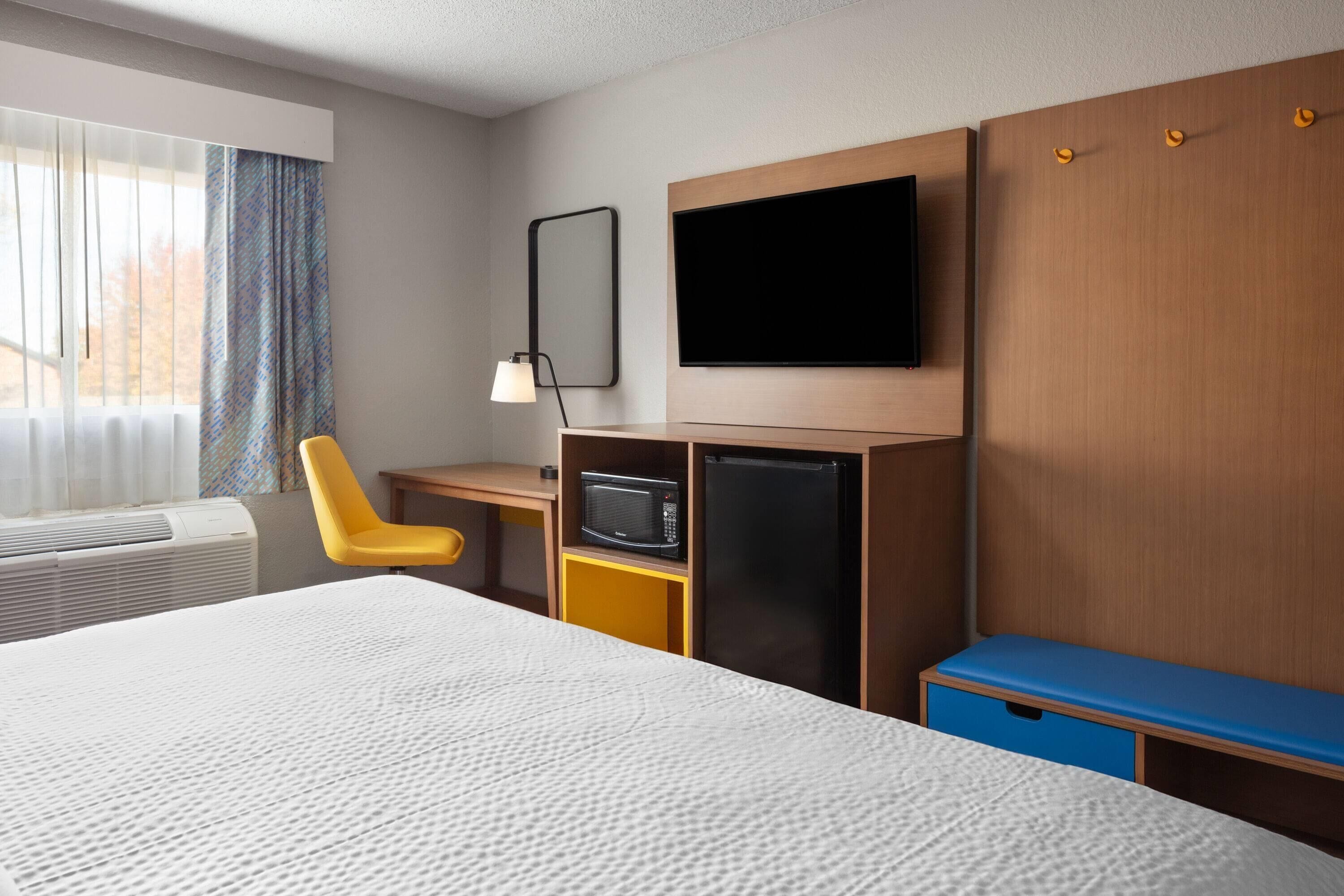 A hotel room with a bed, a desk with a microwave, a TV, and a wardrobe.