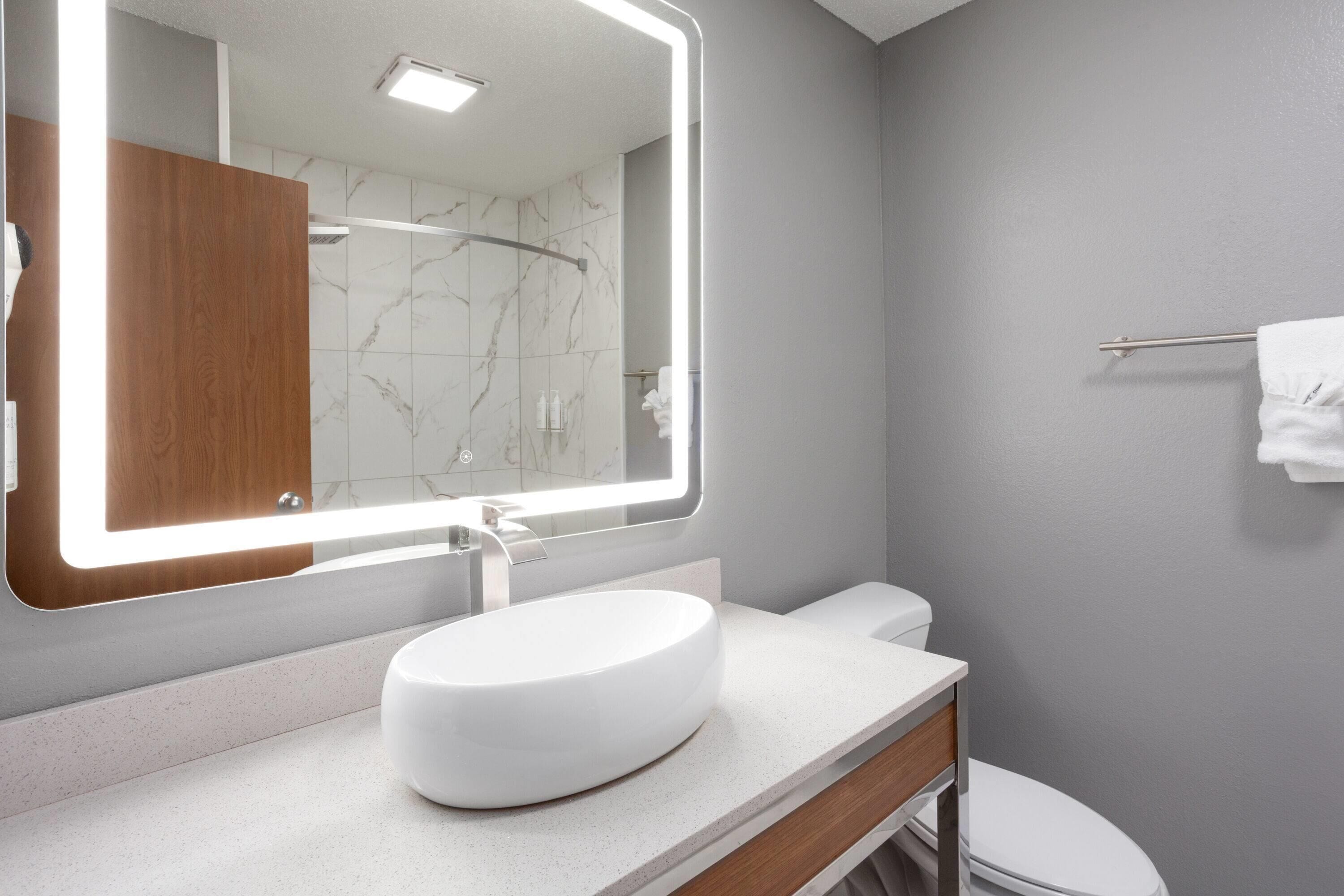 A modern bathroom with a large mirror, white sink, and toilet.