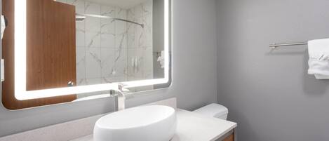 Un baño moderno con un espejo grande, un lavamanos blanco y un inodoro.