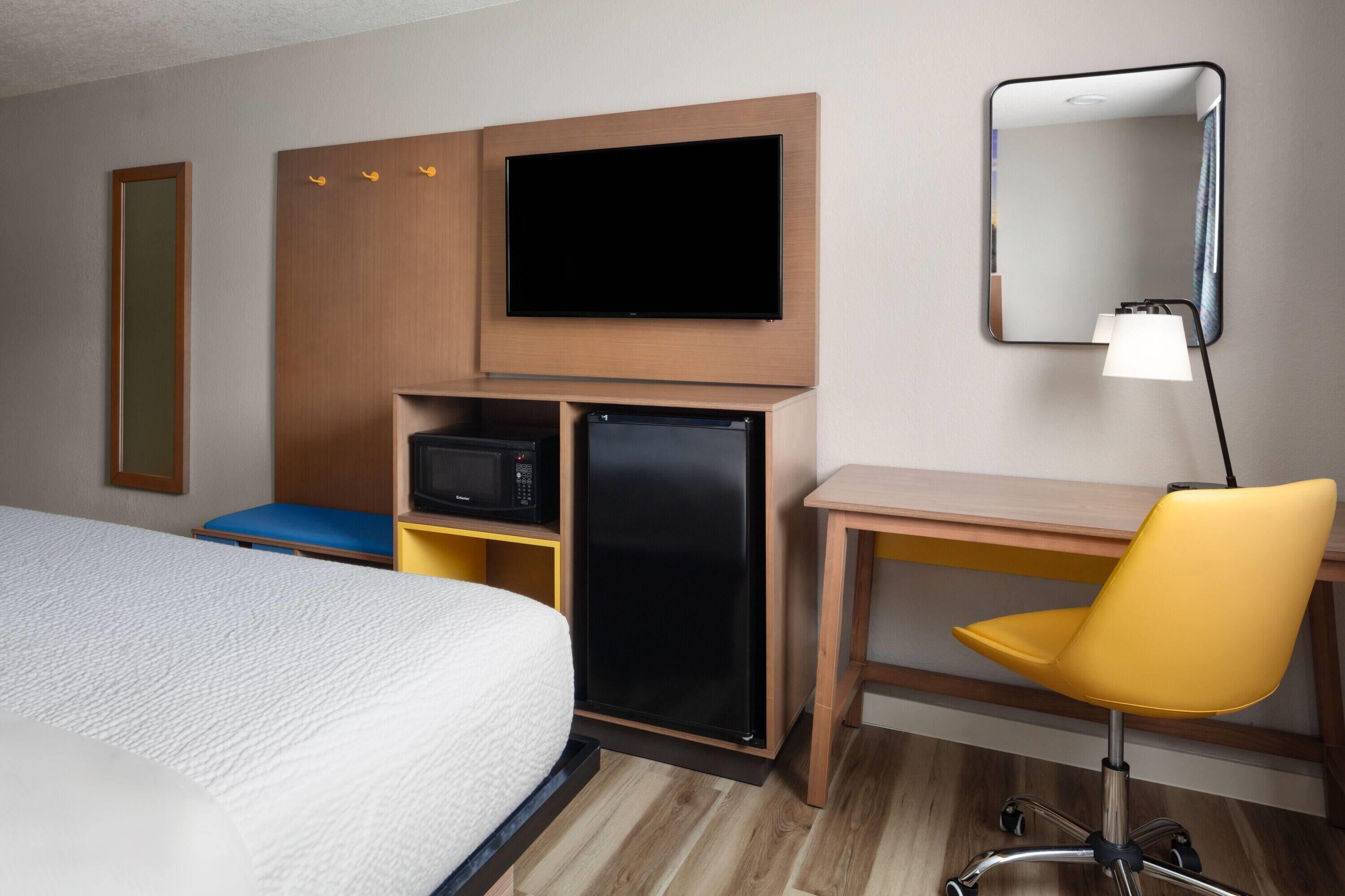 A hotel room with a bed, a desk with a chair, a television, a microwave, and a refrigerator.