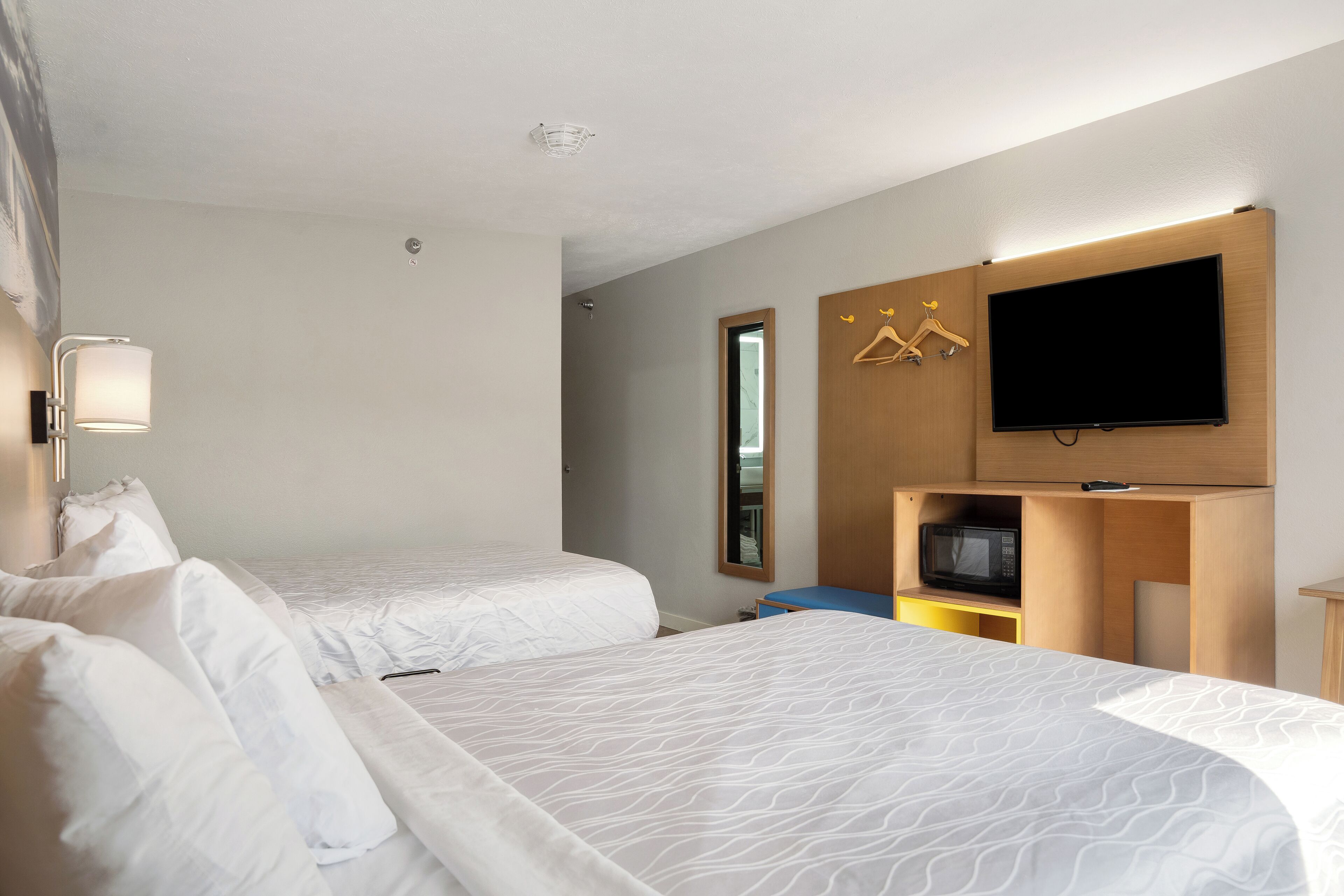 A hotel room with two beds, a TV, a microwave, and a wooden cabinet.