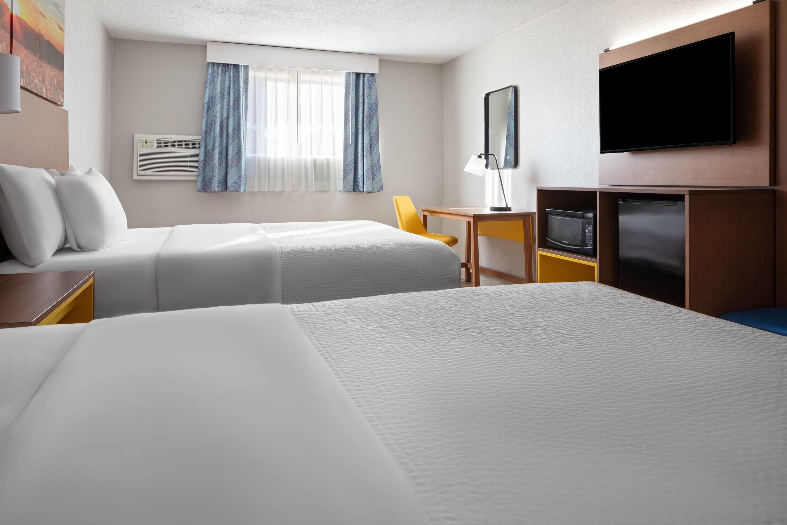 Une chambre d’hôtel avec deux lits, un bureau, une chaise, une télévision, un four à micro-ondes et un réfrigérateur.