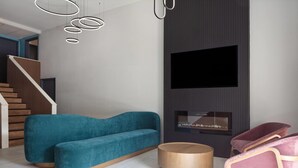 Una sala de estar moderna con un sofá azul verdoso, una mesa redonda de madera y una silla rosa.