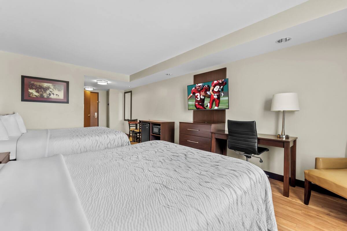 A hotel room with two beds, a desk, a TV, and a chair.