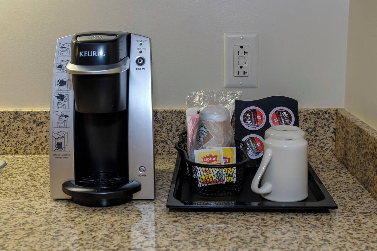 A Keurig coffee maker with a drip tray, a Lipton tea box, and a white mug on a granite countertop.