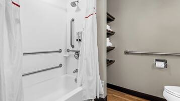 Une salle de bain avec une baignoire blanche, des barres d’appui, une douche avec un pommeau de douche amovible, des toilettes et un porte-serviettes.
