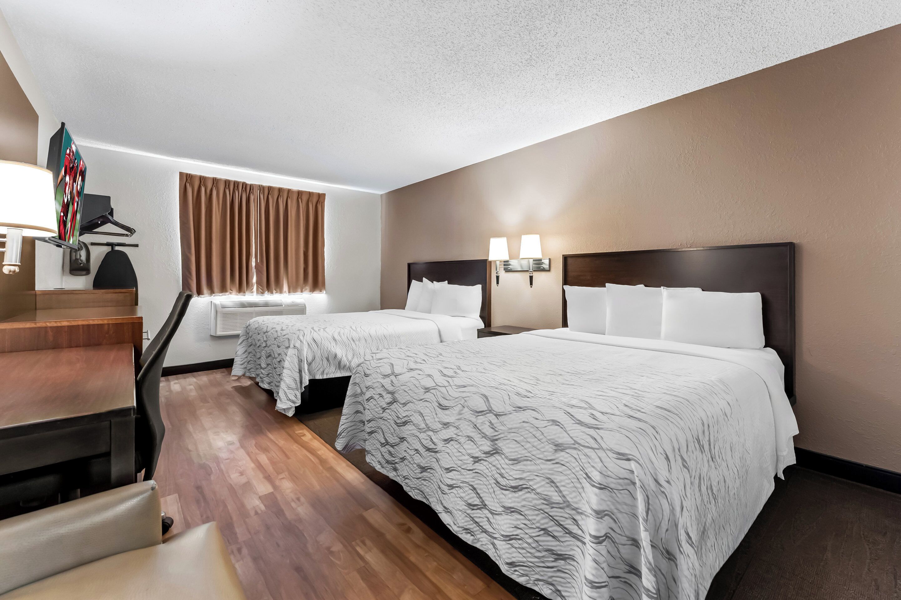 Ein Hotelzimmer mit zwei Betten, einem Schreibtisch und einem Stuhl.