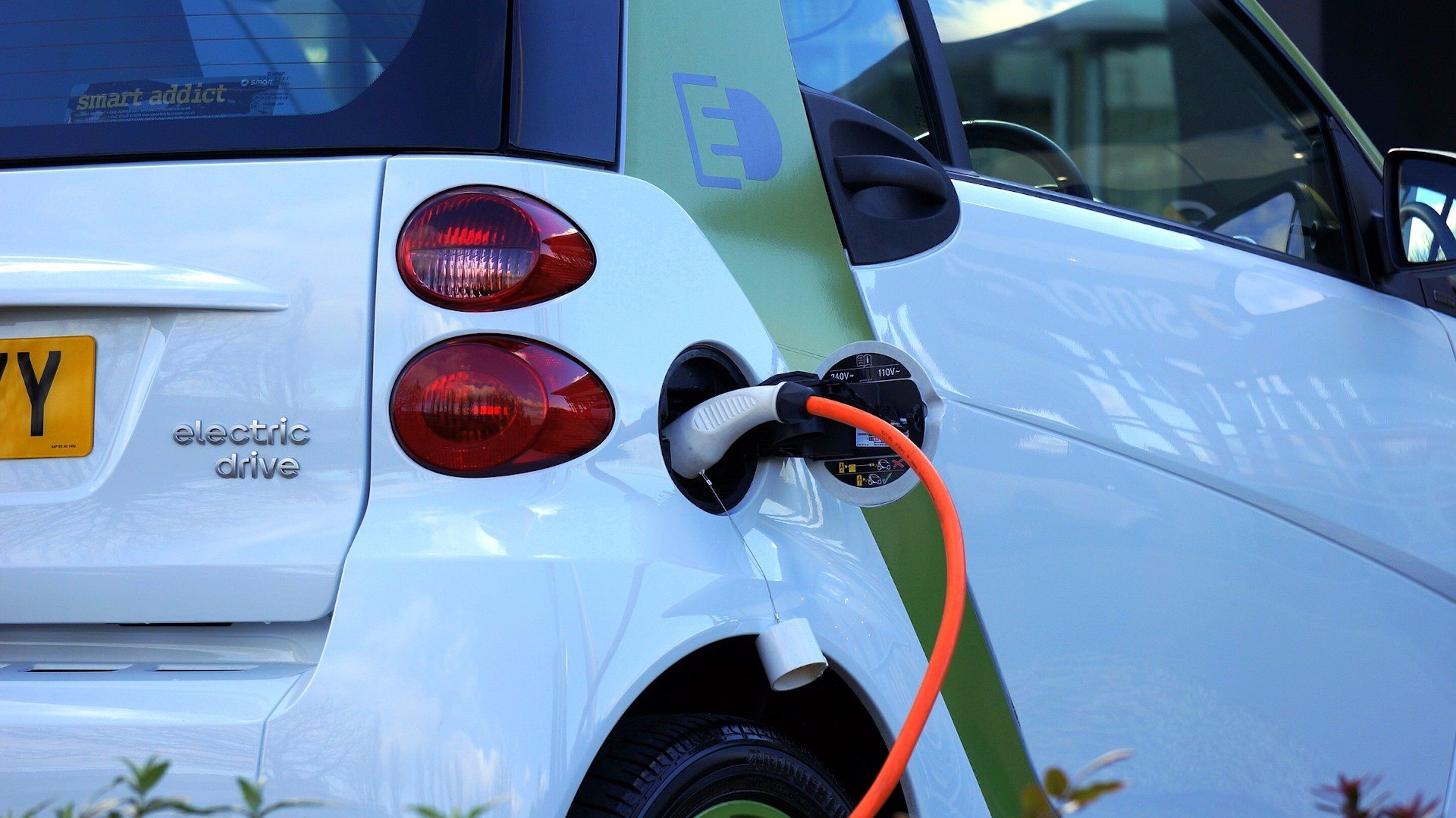 Ein weißes Elektroauto mit angeschlossenem Ladekabel an einer Ladestation.