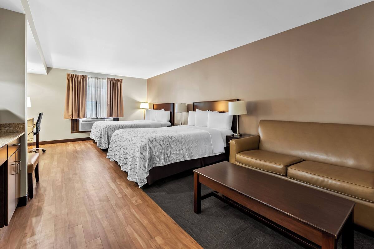 A hotel room with two beds, a sofa, a desk, and a chair.
