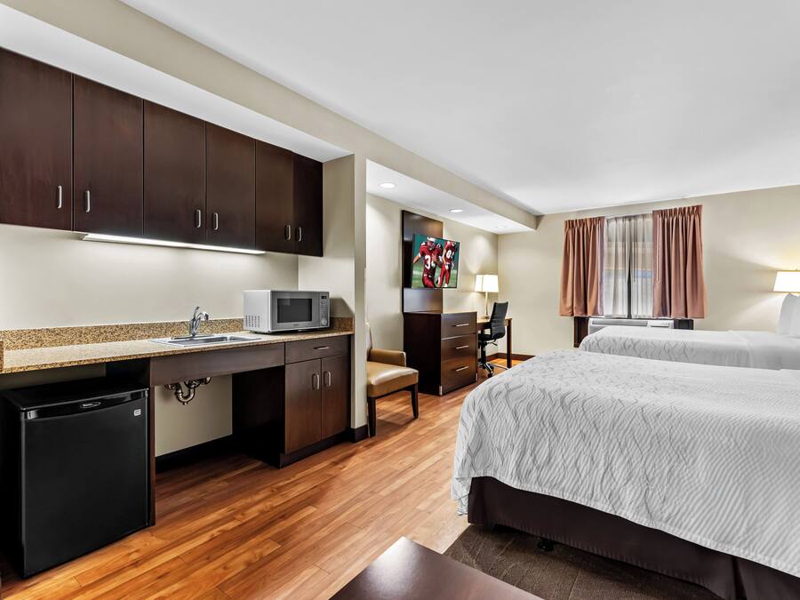Een hotelkamer met een kitchenette, een bed, een bureau en een televisie.