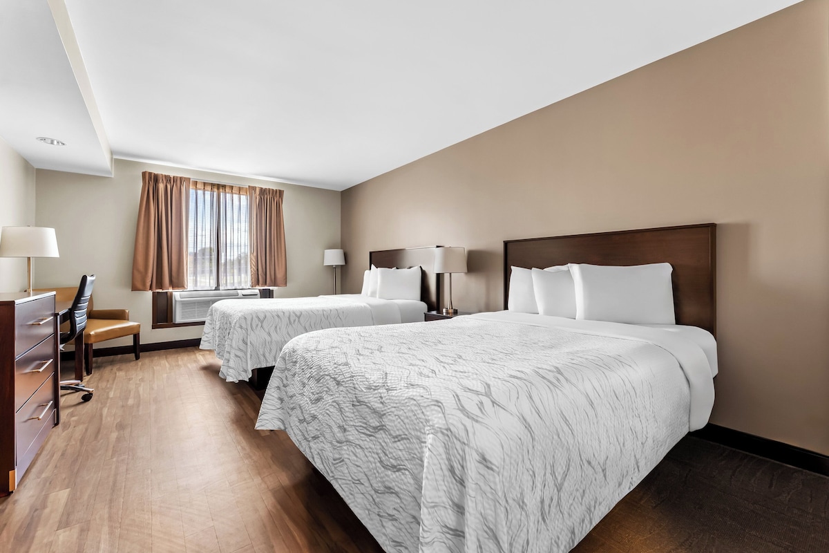 Une chambre d’hôtel avec deux lits, un bureau, une chaise et une fenêtre avec des rideaux.