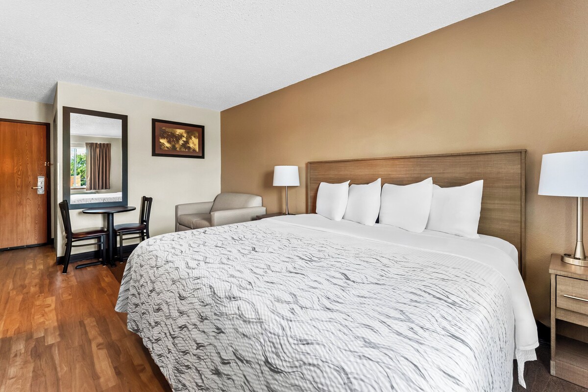 Une chambre d’hôtel avec un grand lit, un bureau avec deux chaises, une petite table et une lampe.