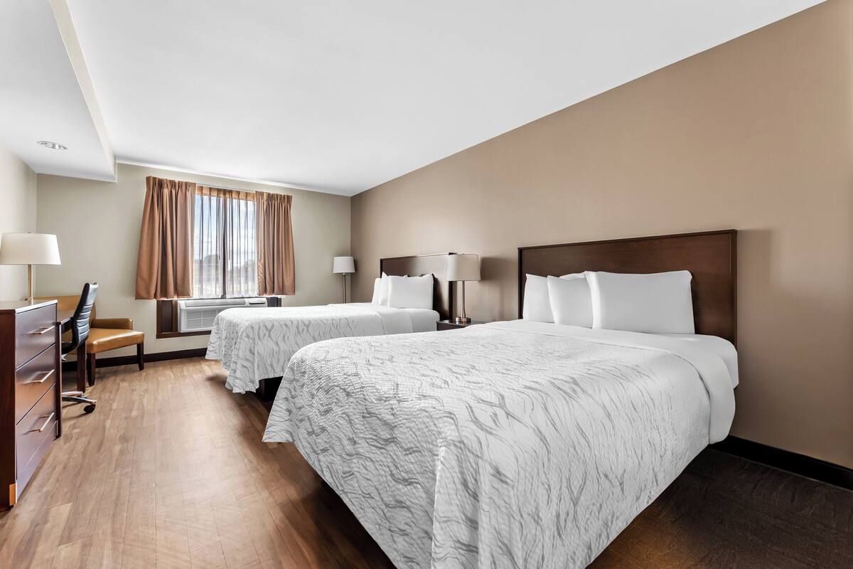 A hotel room with two beds, a desk, a chair, and a window with curtains.