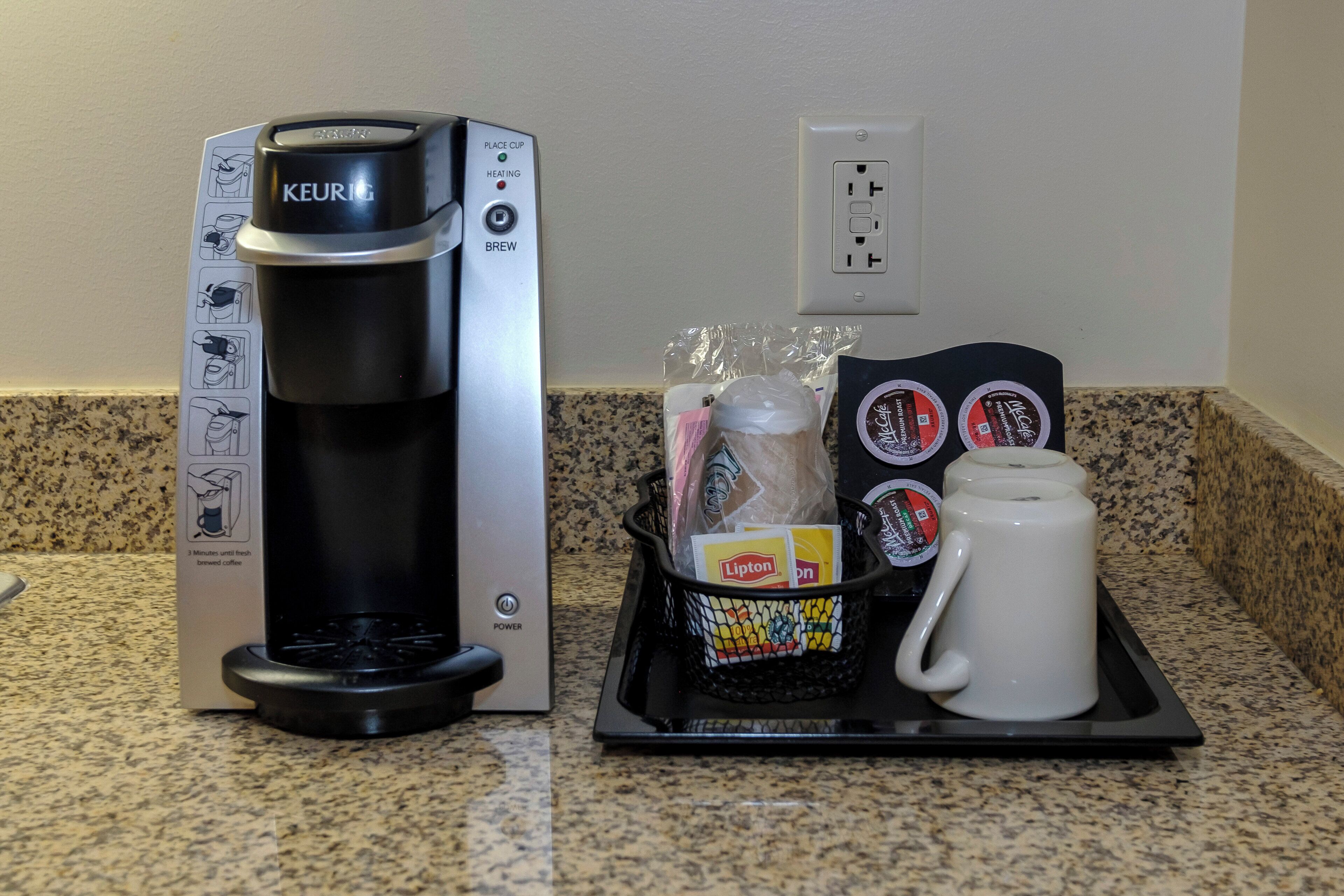 Una cafetera Keurig con una bandeja de goteo, una caja de té Lipton y una taza blanca sobre una encimera de granito.