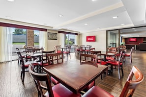 Un vaste espace dédié à la salle à manger, avec de nombreuses tables en bois et des chaises à l’assise rembourrée de tissu rouge, de grandes fenêtres avec des rideaux, et une enseigne rouge indiquant que le Wi-Fi est disponible gratuitement.