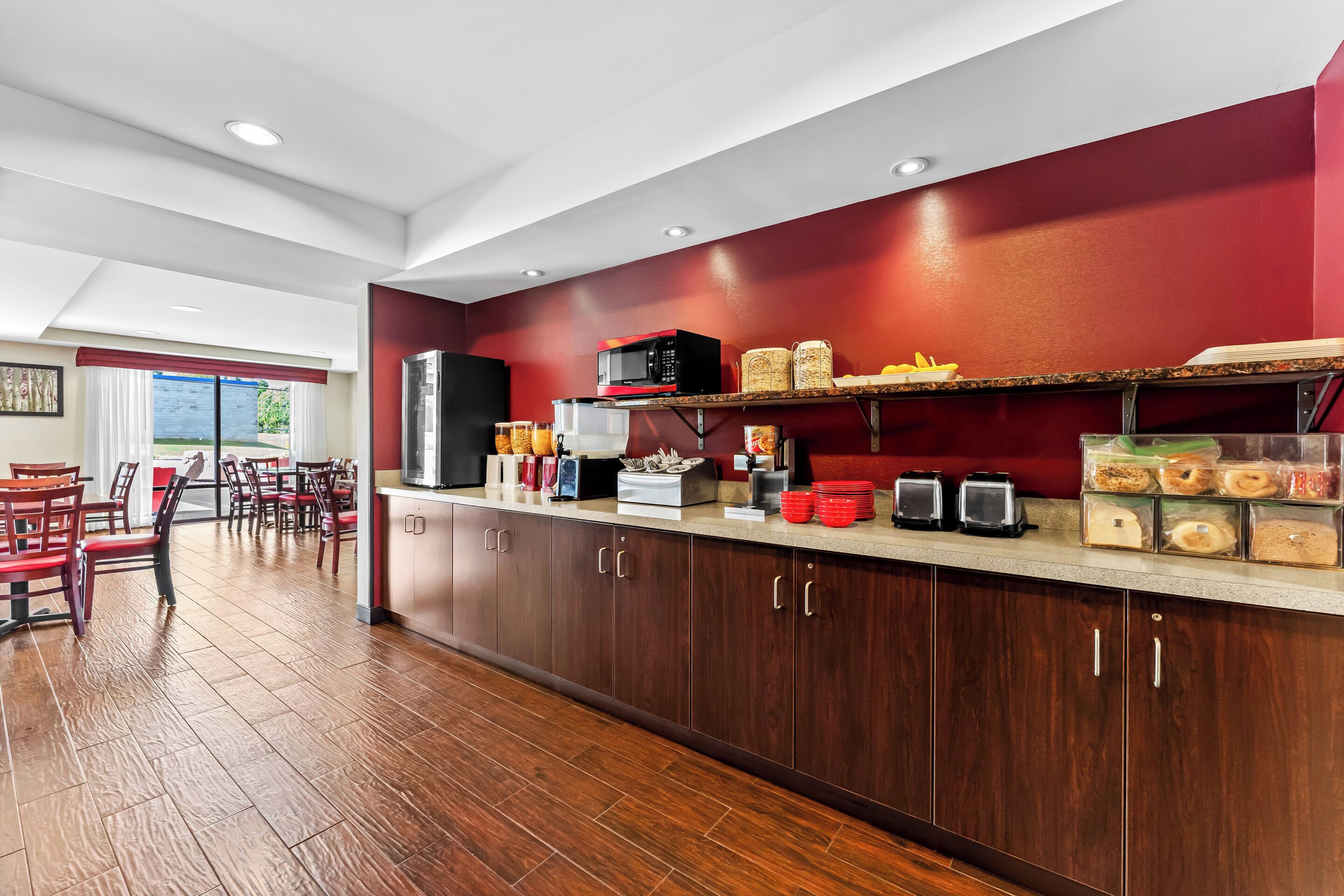 A modern kitchen with wooden cabinets, a microwave, and a breakfast bar with various food items.