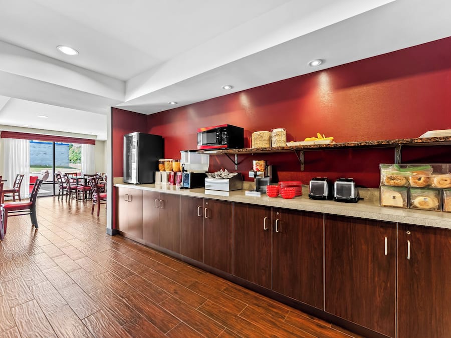 A modern kitchen with wooden cabinets, a microwave, and a breakfast bar with various food items.