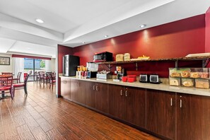 A modern kitchen with wooden cabinets, a microwave, and a breakfast bar with various food items. - Red Roof Inn PLUS+ & Suites Malone (Malone)