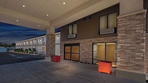 A hotel exterior with a modern design, featuring a brick facade, large windows, and a covered outdoor area with a pool. - Red Roof Inn PLUS+ & Suites Malone (Malone)