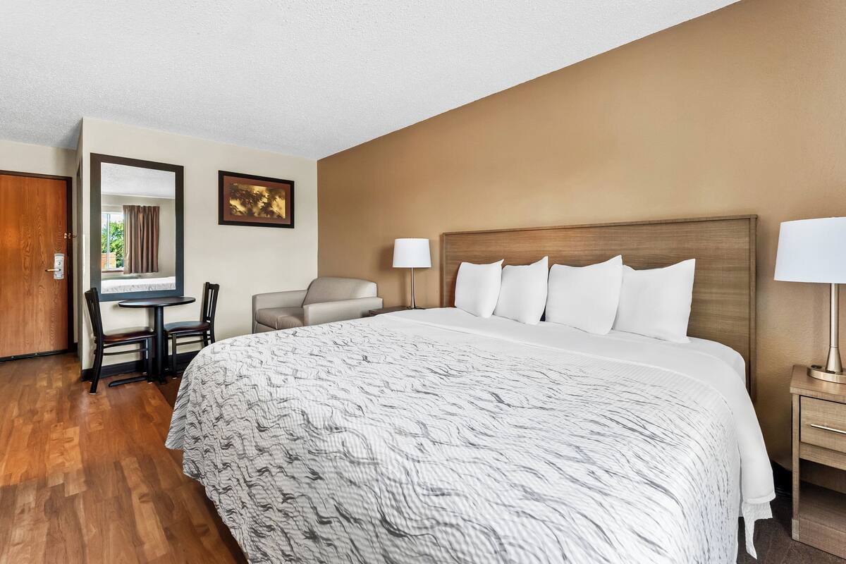 A hotel room with a large bed, a desk with two chairs, a small table, and a lamp.