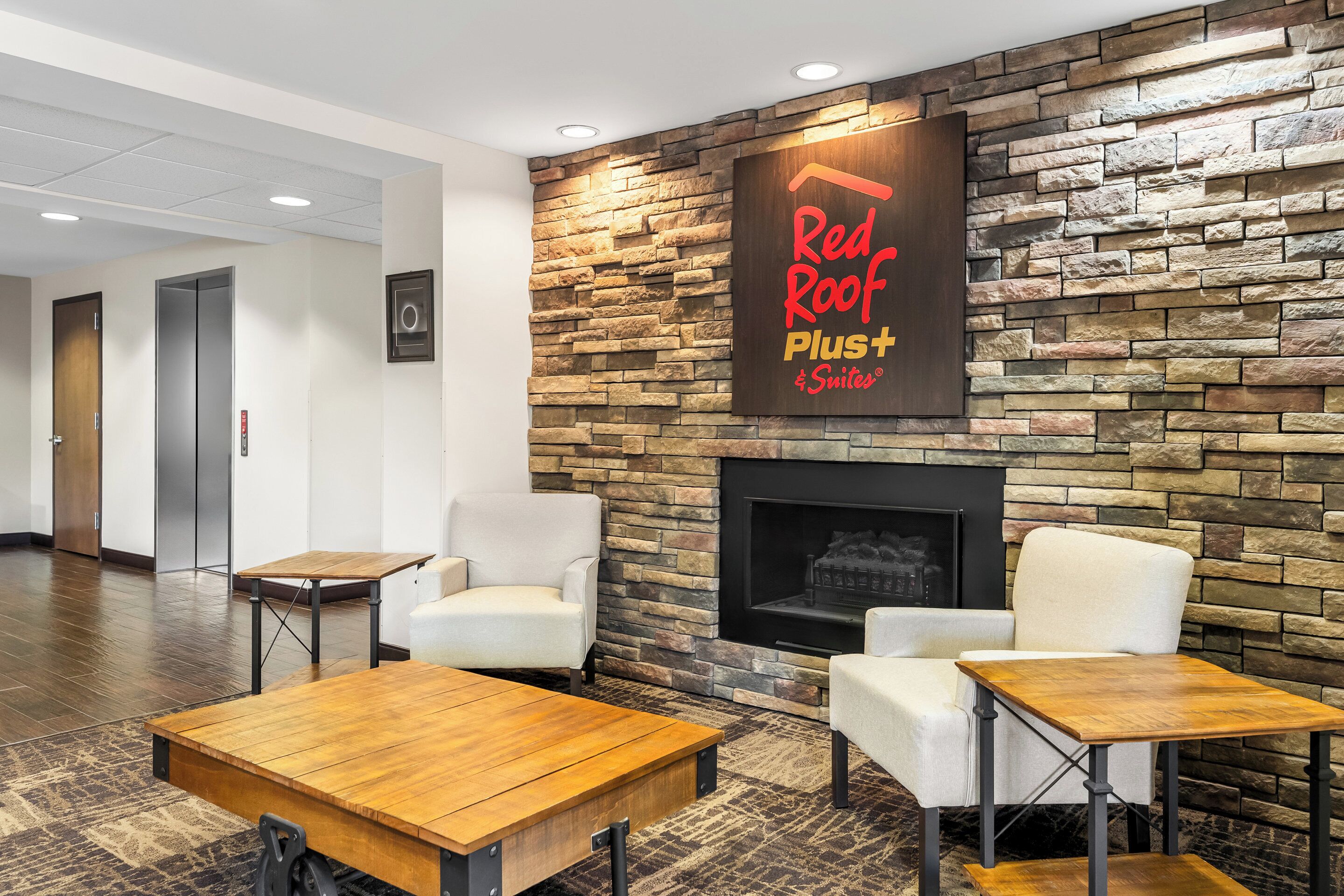 En hotellobby i stil med Red Roof Plus Suites, med en vägg av sten, en öppen spis och en sittgrupp.
