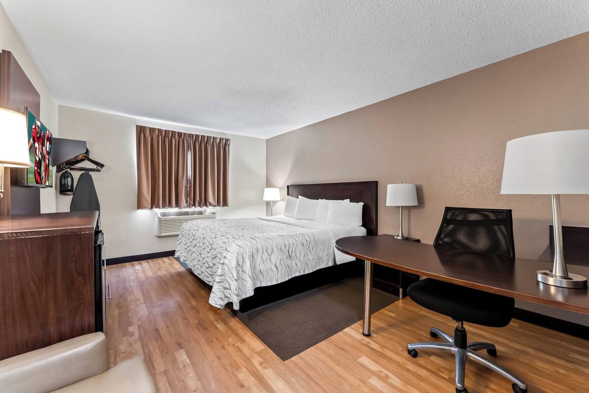 A hotel room with a bed, desk, chair, and two lamps.