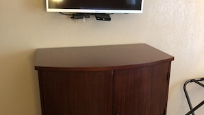 A wooden cabinet with a flat top and two doors, positioned under a mounted television on a wall. - Inn Between The Hedges (Athens)