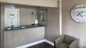 A reception area with a blue counter, a clock, and a patterned armchair. - Inn Between The Hedges (Athens)