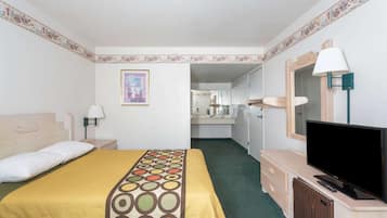 A hotel room with a bed, a TV, a desk, and a bathroom visible through an open door.