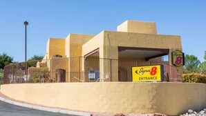 A Super 8 hotel entrance with a yellow facade, a fenced parking area, and a clear blue sky.