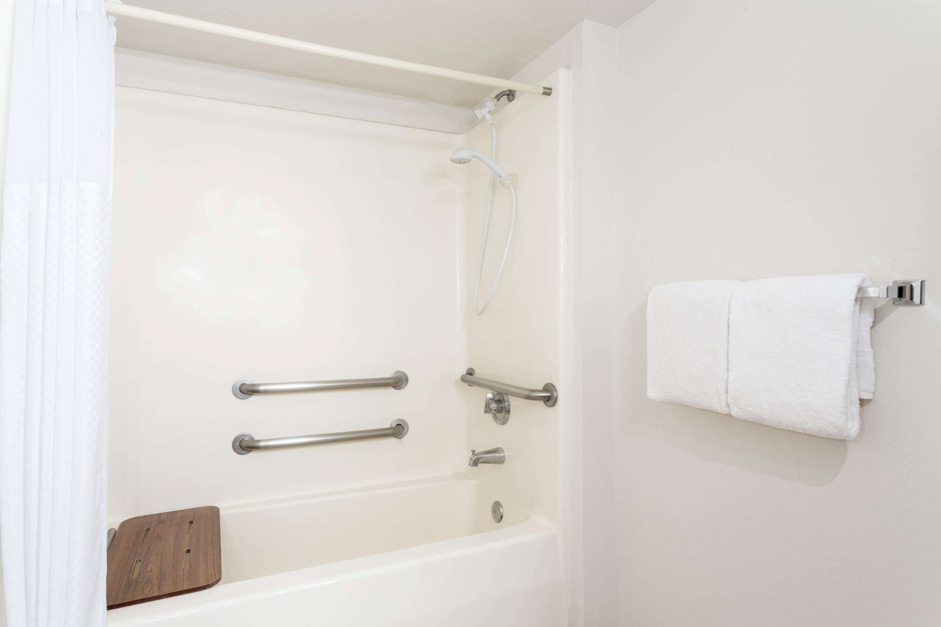 A white bathtub with grab bars, a wooden tray, and a towel rack.