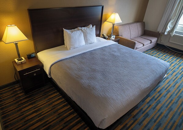 Habitación de hotel con una cama grande, dos lámparas de noche, una mesita de noche, una silla y piso alfombrado.